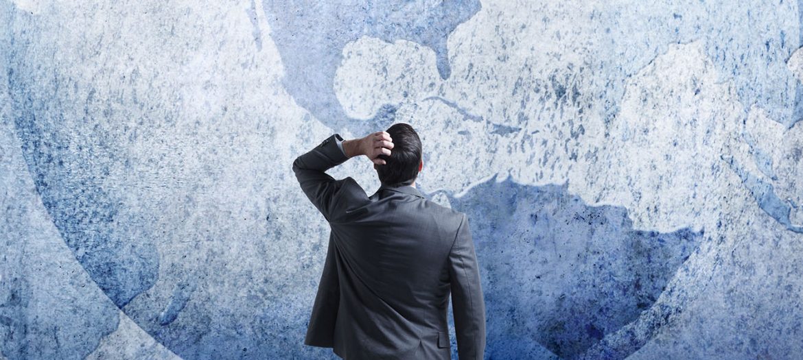 Businessman Stands And Looks Up At Three Interlocking Globes On Wall